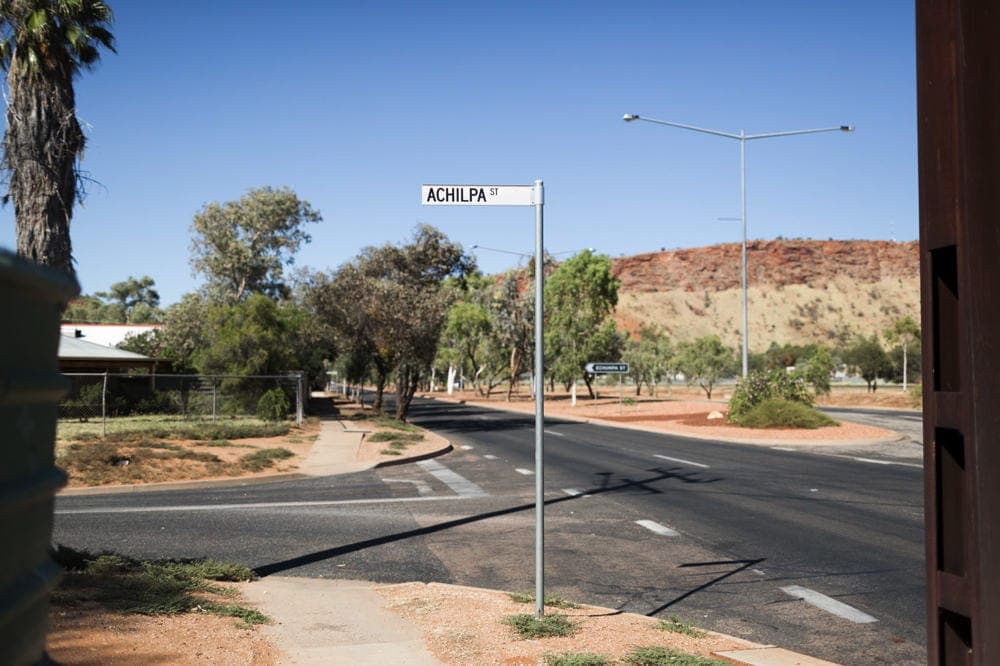 An Achilpa Street sign at a quiet intersection with red earth and a ridge in the background.